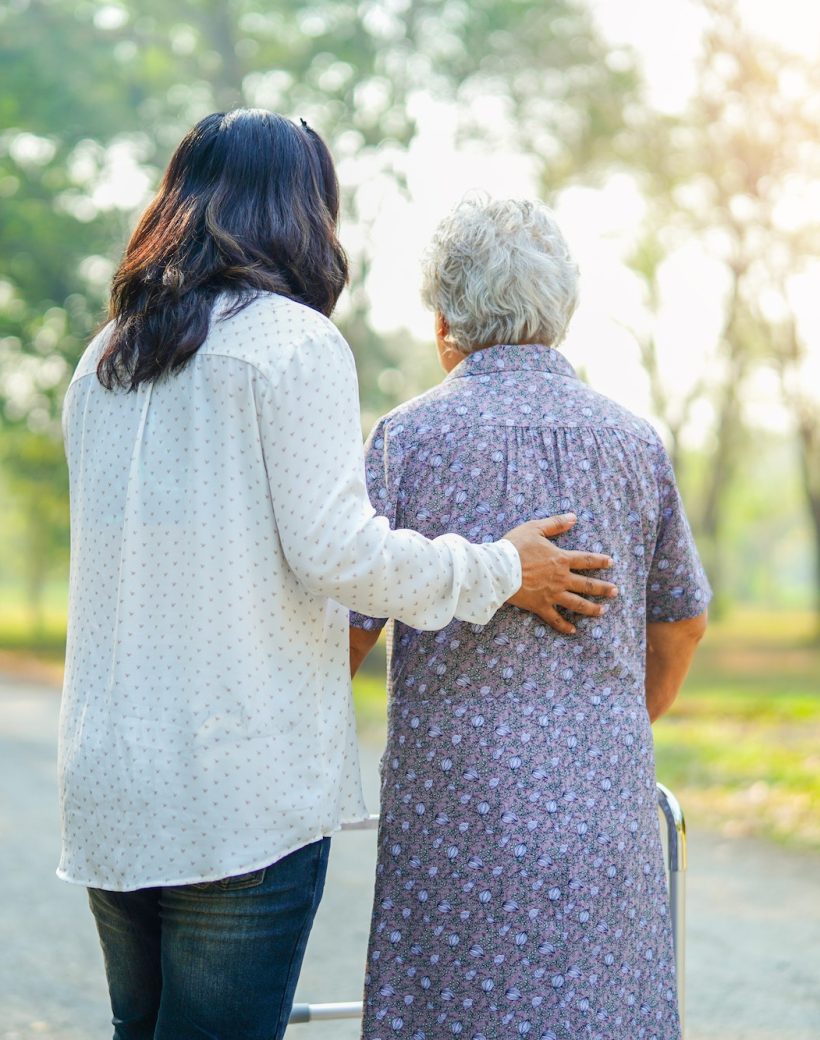 Altenpflegerin geht mit einer älteren Frau durch einen Park